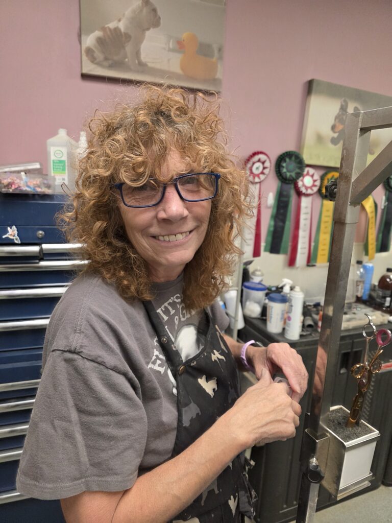 A smiling woman with curly hair and glasses working in a workshop.